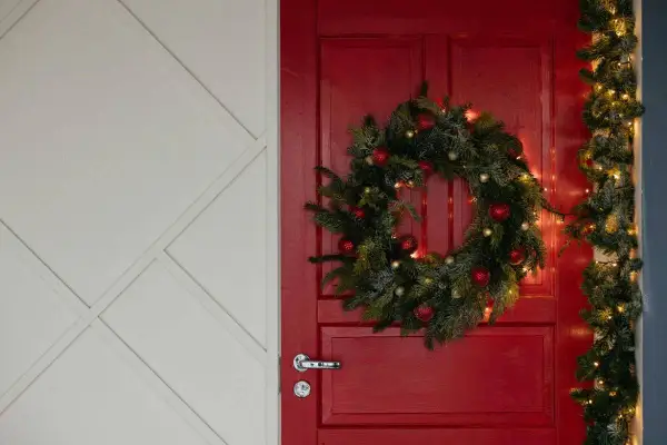 Un ingresso natalizio da sogno: una porta rossa con ghirlanda di pino, palline rosse e luci dorate per abbellire porta ingresso natale.