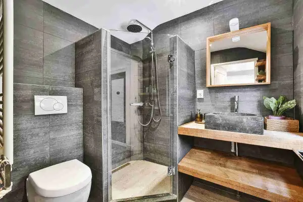 Bagno grigio chiaro e bianco con doccia in vetro, lavabo in pietra e specchio in legno.
