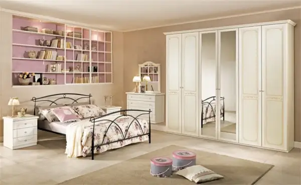 Camera da letto classica: letto in ferro battuto, armadio bianco con specchi, cassettiera e libreria a muro.