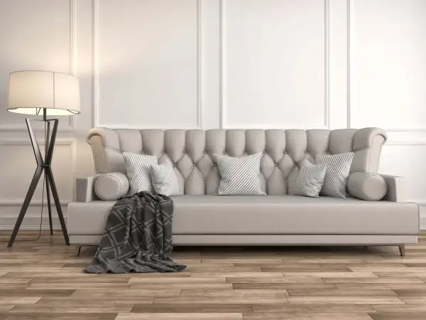 Divano imbottito beige con cuscini a righe grigie e una coperta scura. La lampada da terra nera completa l'arredamento, dimostrando che beige e grigio stanno bene insieme.