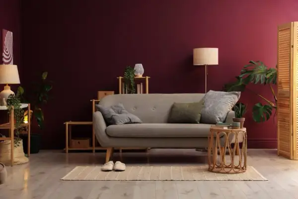 Soggiorno accogliente con divano grigio, piante verdi e pareti color vinaccia intenso.