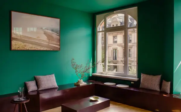 Un soggiorno moderno con pareti verde smeraldo, un quadro astratto, un divano basso in legno scuro e cuscini a quadri. I colori che stanno bene con il verde sono esaltati dal contrasto.