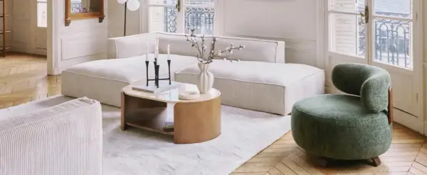 Tavolino con finitura in legno betulla colore, accanto a un divano bianco e una poltrona verde.