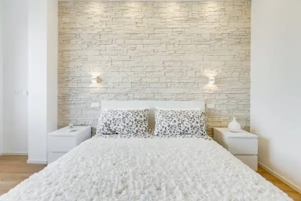 Accogliente camera da letto moderna con una suggestiva parete in pietra che fa da sfondo al letto.