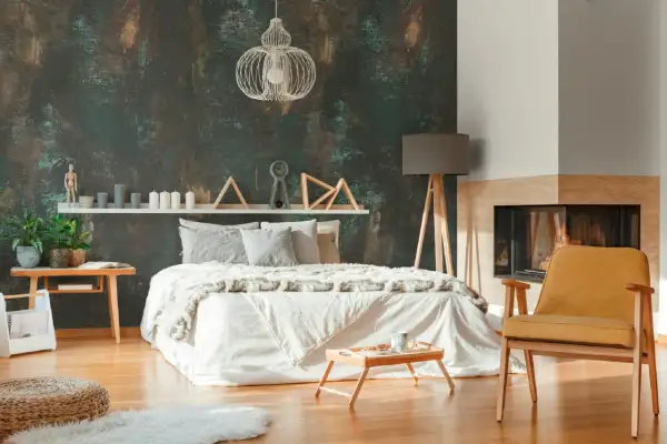 Camera da letto con carta da parati effetto materico e pittura chiara, letto bianco, camino e poltroncina gialla.