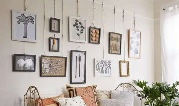 Una galleria di quadri appesi in modo originale con corde, tra cui una palma, conchiglie e piume.