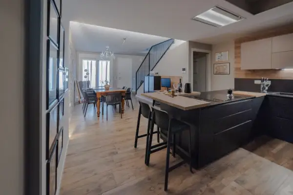 Elegante cucina soggiorno open space di 30 mq con isola nera, tavolo da pranzo in legno e scala moderna.