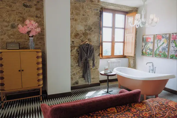 Un bagno rustico chic con vasca freestanding color pesca, pareti in pietra, un accappatoio appeso e un mobile in legno.
