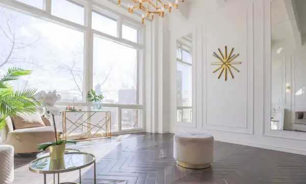 Un elegante soggiorno con un divano beige, tavolini rotondi in vetro e oro, e un orologio da parete dorato. Grigio e oro stanno bene insieme, creando un'atmosfera sofisticata.