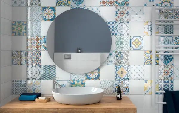 Bagno con lavabo su mobile in legno, specchio rotondo e pareti decorate con vivaci cementine bagno dai motivi geometrici e floreali.